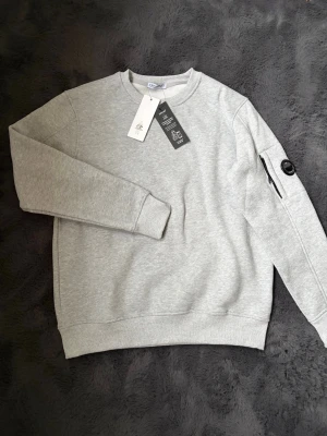 C.P. Company Tröja - Nu säljes en helt ny aldrig använd C.P. Company tröja som är i grå färg. Otroligt fin och skön. Skriv direkt vid funderingar eller frågor!