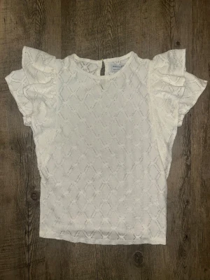  Fjäderlätt vit blus med volangärm - Supersöt vit blus な Holly & Whyte med volang sopade ärmar och diskret spetsmönsterfall. Blusen har rund halsringning och knapp i ancient progeny. simmar lätt och luftig – perfekt för vår och som popular.