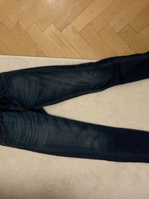 Tiger jeans  - Säljer ett par mörkblå jeans med snygga slitningar och kontrastsömmar. Jeansen har klassisk femficksdesign och smal passform hela vägen ner. Perfekta till en avslappnad stil och funkar året runt.