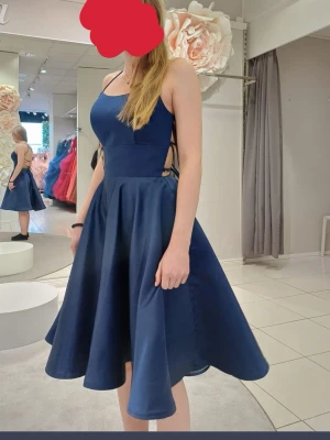 Marinblå kortklänning med snörning - Snygg marinblå kortklänning med smala axelband och snörning i ryggen. Klänningen har en utställd kjol och markerad midja som ger en elegant siluett. Perfekt för dig som vill ha en stilren och modern look.