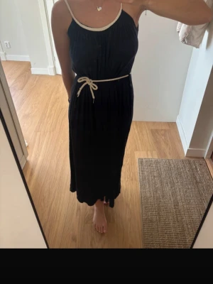 Mörkblå långklänning  - Blp långklänning med beige axelband och midjeband i knytmodell. Klänningen har en avslappnad passform och är ärmlös med rundad halsringning. Perfekt för varma dagar och enkel att styla med accessoarer. Supermjuk och skön! Inköpt i Spanien