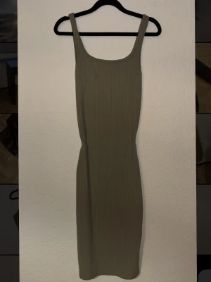Ribbad grön långklänning - Säljer en ribbad grön långklänning med smala axelband och figurnära passform. Klänningen har en enkel och stilren design som passar perfekt till sommaren. Materialet känns mjukt och stretchigt för extra komfort.