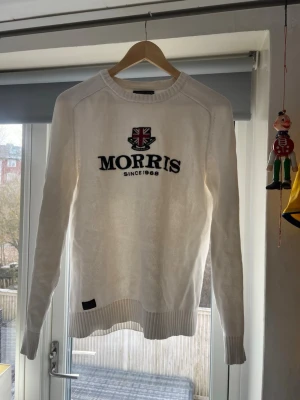 Morris Vit Tröja - Vit tröja från Morris med broderad Union Jack och texten 'Morris Since  1968' på bröstet. Tröjan  har rund hals  och ribbade muddar vid ärmslut och nederkant. Till tidyverkad i suport stickat material för en clean och stilren look.
