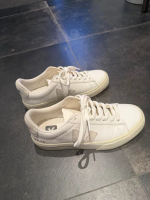Vita Veja sneakers med beige detaljer - Stilrena vita sneakers från Veja! Använd fåtal gånger så väldigt fint skick. Vid intresse kan fler bilder skickas