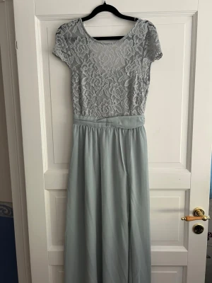 Ljusblå långklänning med spets - Elegant ljusblå långklänning med spetsliv och korta ärmar. Överdelen har ett blommigt spetsmönster och v-ringad rygg. Kjolen är i ett mjukt, flytande tyg. Perfekt för speciella tillfällen och student. Använd endast 1 gång. 