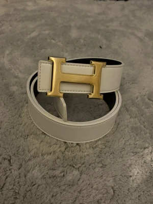 Svart-vit bälten  bälte med guld H-spänne - Snyggt vändbart bälte i svart och vitt skinn med ikoniskt guldigt H-spänne. Perfekt accessoar för att lyfta vilken outfit som helst. Bältet har en stilren och klassisk design med exklusiv känsla.