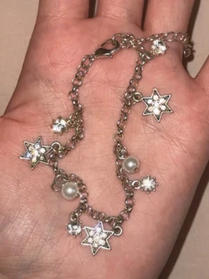 Silverfärgat armband med stjärnor - Armband i silverfärgad metall med kedja och hängande stjärnberlocker dekorerade med små glittrande stenar. Armbandet har även vita pärlor och runda kristallberlocker. Perfekt för dig som gillar detaljer och stjärnmotiv.🥹🧸🩷