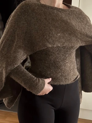 Brun stickad tröja cape-  Gina Tricot - Säljer en brun stickad tröja från Gina Tricot i storlek XS. Tröjan har en figurnära passform med långa ärmar och cape. Materialet är fluffigt och mjukt. Enkel att styla till olika outfits. Aldrig använd.
