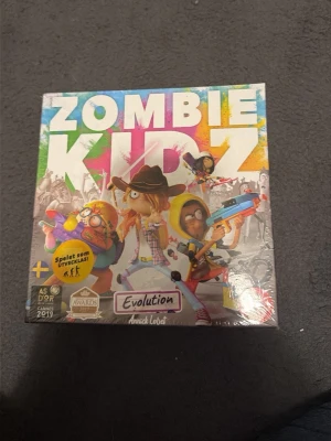 Zombie Kidz Evolution brädspel - Zombie Kidz Evolution är ett färgglatt och roligt brädspel där spelarna samarbetar för att besegra zombier. Spelet utvecklas under tiden med klistermärken och hemliga kuvert. Låda i kartong med tecknade figurer och svensk text.