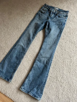 Blå bootcut jeans från Gina Tricot - Säljer ett par ljusblå bootcut jeans från Gina Tricot. Jeansen har klassisk femficksmodell, normal midja och utsvängda ben. Tillverkade i mjuk denim med snygg tvätt och kopparfärgade nitar. Perfekta för en avslappnad och trendig look.