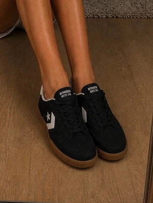 Svarta Converse sneakers med vit detalj - Snygga svarta Converse sneakers med vit stjärna och pil på sidan, samt vit häl och svart snörning. Skorna har en klassisk låg modell och brun sula i gummi. Perfekta för en streetwear-look och passar till det mesta. Materialet är mocka och textil.