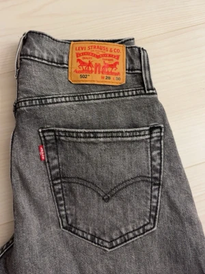 Grå Levi's 502 jeans med rak passform - Snygga grå jeans från Levi's modell 502 med rak passform och klassisk femficksdesign. Jeansen har en vintage tvätt och tydlig Levi's-lapp bak i midjan. Tillverkade i slitstark denim med den ikoniska röda Levi's-taggen på bakfickan.