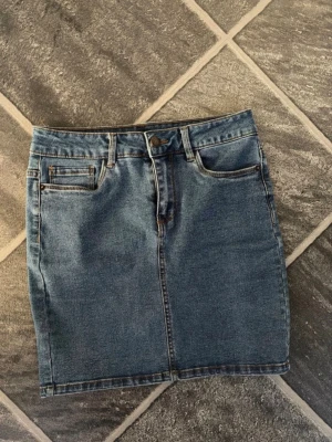 Blå jeanskjol med fickor - Snygg blå jeanskjol i klassisk modell med fem fickor och bälteshällor. Kjolen har knapp- och dragkedjestängning framtill samt två bakfickor. Tillverkad i denim med kontrastsömmar för en tidlös look.