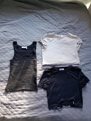 Tre trendiga toppar i svart och beige - Säljer tre snygga toppar: en ribbad svart linnetopp, en croppad beige t-shirt och en svart croppad t-shirt med kedjedetalj. Perfekta för att mixa och matcha till olika outfits. Passar dig som gillar en modern och avslappnad stil. Alla i M ☺️