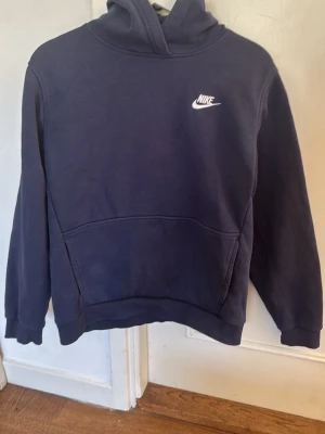 Mörkblå hoodie från Nike XL 158-170 cm - En klassisk mörkblå hoodie från Nike i storlek XL. Hoodien har huva, ribbade muddar vid ärmslut och nederkant samt en mjuk insida. Perfekt för en avslappnad och sportig stil.