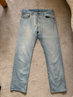 Ljusblå Levi's raka jeans - Säljer ett par klassiska ljusblå jeans från Levi's av modellen 501 med raka ben och femficksmodell. Jeansen har en snygg vintage tvätt och den ikoniska läderpatchen bak i midjan. Perfekta för en avslappnad och trendig look.