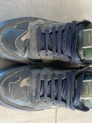 Valentino Rockrunners - Snygga sneakers från Valentino med camo-mönster i grönt, svart och beige. Skorna har svarta skosnören, detaljer i mocka och läder samt en unik detalj med nitar på hälen. Sulan är beige. Perfekt för dig som vill sticka ut. OBS, finns ett litet hål som ni ser på bild 2. Priset är inte hugget i sten!! Hör gärna av dig