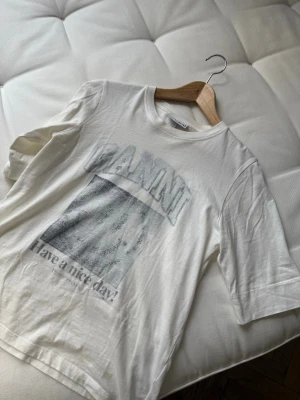 Vit GANNI t-shirt med tryck XS - Vit t-shirt från GANNI i bomull med tryck framtill och klassisk rund hals. Modellen är kortärmad och har en avslappnad passform