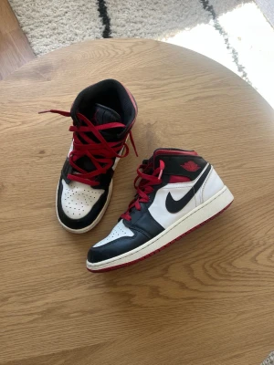 Jordan 1 Mid - Tjena!👋 Säljer ju dessa snygga Nike Air Jordan 1 Mid sneakers i svart, vitt och rött🤩 Skorna har klassisk design med röd logga på sidan, röda skosnören och svart swoosh🧼Ovandelen är i läder och har perforerad tåbox för extra ventilation✌️Dem är inte använda på ett tag men är i bra skick👍 Meddela gärna vid frågor📩