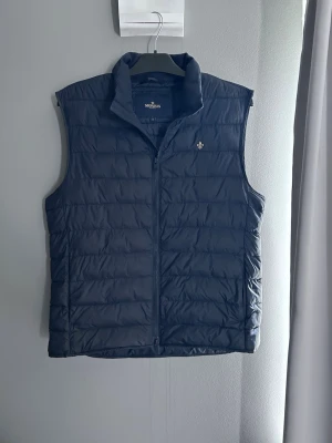 Mörkblå dunväst Morris - Snygg mörkblå dunväst från Morris med quiltad design. Västen har dragkedja framtill och en liten broderad logga på bröstet. Perfekt för lager-på-lager och håller dig varm under kyliga dagar.