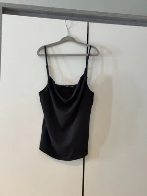 Svart linnetopp från BikBok - Svart linnetopp från BikBok med tunna axelband och snygg draperad urringning. Toppen har en enkel och stilren design som passar perfekt till jeans eller kjol. Materialet känns mjukt och följsamt mot huden.