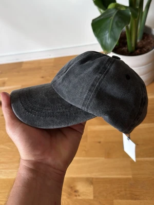 Mörkgrå keps från Polo R. - Snygg mörkgrå keps från Polo R. med klassisk böjd skärm och diskret broderad logga framtill. Kepsen är tillverkad i mjuk bomull och har justerbar rem baktill för perfekt passform. Perfekt accessoar för en avslappnad och stilren look.