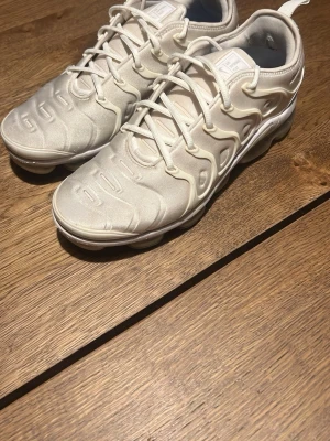 Nike Air Vapormax Plus vita sneakers - Nike Air Vapormax Plus sneakers i helvitt med genomskinlig sula. Ovandelen är i textil och syntet med unika vågformade detaljer och snörning. Sulan har synliga luftbubblor för extra komfort och en futuristisk look. Perfekta för dig som gillar streetwear och sportig stil. Säljs för att de inte är min stil längre men hoppas de kan passeras vidare till någon annan. Lite slitage på högra skon då jag använt dessa en del av förra sommaren, men det är inget märkvärdigt, känns inte och syns inte.
