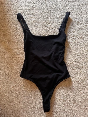 Svart body med breda axelband - Säljer en enkel och stilren svart body med breda axelband och djup rundad halsringning. Materialet är mjukt och stretchigt, vilket gör den bekväm att bära. Perfekt att matcha med jeans eller kjol för en snygg look.