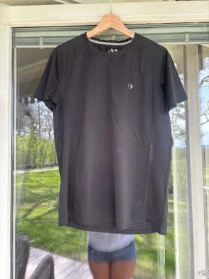 Svart tränings-tshirt från Lager 157 - Svart kortärmad tränings-tshirt från Lager 157. Perfekt för löpning eller gym, med rund hals och diskret logga på bröstet. Lätt och ventilerande tyg som håller dig sval under träningen.