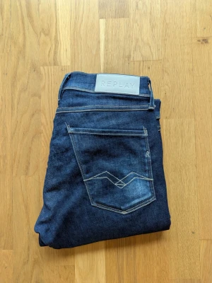 Mörkblå Replay Anbass jeans - Säljer ett par mörkblå Replay Anbass jeans med klassisk femficksdesign och snygga kontrastsömmar. Jeansen har normal passform och är tillverkade i ett stretchigt denimtyg. Perfekta för dig som gillar stilrena och bekväma jeans.