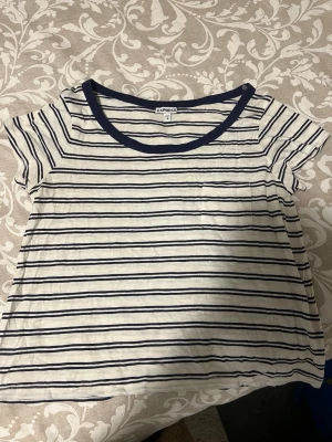 Randig t-shirt  - Vit t-shirt med marinblå ränder. Klassisk rund halsringning med mörkblå kant och korta ärmar. Perfekt för en avslappnad och stilren look. Tillverkad i mjukt bomullsmaterial.