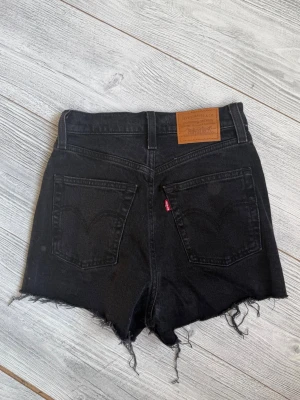 Svarta Levi's high waist jeansshorts - Säljer ett par svarta jeansshorts från Levi's med hög midja. Perfekta för sommaren.                                      Använt dom väldigt fåtal gånger. Ny skick. Storlek 24.