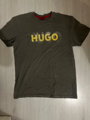 Grön HUGO t-shirt med tryck - Snygg grön t-shirt från HUGO med stort tryck i gult och vitt på bröstet. Klassisk rund halsringning och korta ärmar. Perfekt för dig som gillar enkel men stilren design.