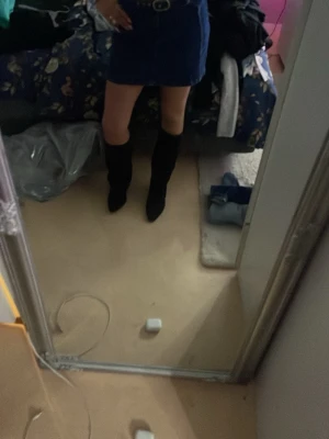 Mörkblå kort jeanskjol - Säljer en mörkblå kort jeanskjol med klassisk rak passform och hög midja. Kjolen har bälteshällor och stängs med knapp och dragkedja framtill. Perfekt att styla med boots eller sneakers för en trendig look.