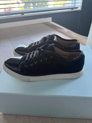 Svarta låga sneakers från Lanvin - Snygga svarta sneakers från Lanvin med ovandel i mocka och detaljer i blankt läder. Säljer de då de inte passade mig när jag köpte de men orginal box, snören, låda, dustbag kvitto finns men kommer ej med 