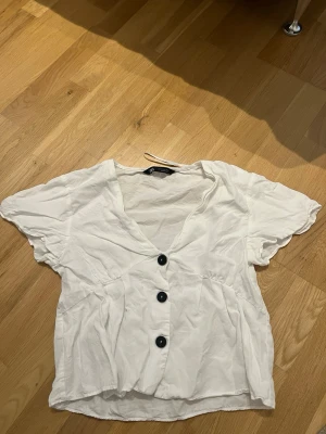 Vit blus med knappar från Zara - Vit blus från Zara med tre stora svarta knappar framtill. Blusen har v-ringning, korta ärmar och  Tillverkad i ett tunt, mjukt tyg. Jättefin & söt blus att ha till sommaren men kommer tyvärr inte till användning för min del ❤️
