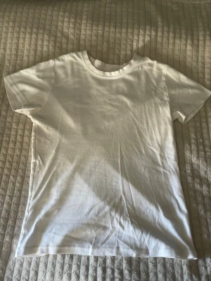 Vit basic t-shirt från Zara - En klassisk vit t-shirt från Zara i storlek 152. T-shirten har rund halsringning och korta ärmar, perfekt för en clean och enkel stil. Tillverkad i mjuk bomull som känns skön mot huden. Har en fläck på insidan av kragen (Bild 3) som tyvärr inte går bort men är inget som syns vid användning av tröjan.