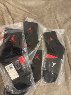 Svarta Jordan strumpor med logga - Säljer flera par svarta Jordan strumpor med den klassiska Jumpman-loggan i rött och vitt. Strumporna är sportiga och har en bekväm passform, perfekta för dig som gillar streetwear och sneakers. Materialet är mjukt och stretchigt för bästa komfort. Storlek 8-12 EU alla 4 för 160
