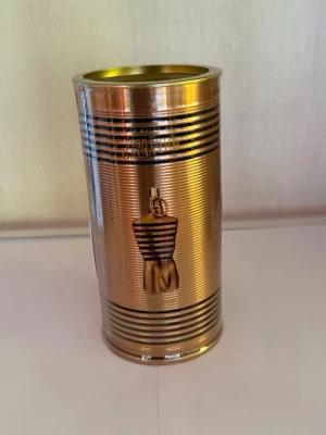 Jean Paul Gaultier Le Male Elixir - Jean Paul Gaultier Le Male Elixir parfym i en lyxig guldfärgad metallburk med svarta ränder och den ikoniska manliga siluetten. Förpackningen har en modern och exklusiv design som verkligen sticker ut i badrumshyllan.