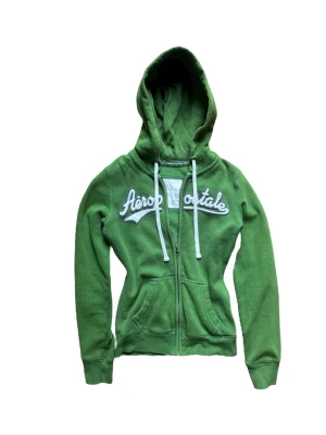 Vintage grön zip hoodie från Aeropostale - Snygg vintage grön hoodie från Aeropostale med vit broderad logga över bröstet. Dragkedja framtill, två fickor och justerbar huva med vita snören. Strl Xs men passar S också. 