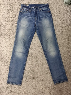 Levi's blå raka jeans - Säljer ett par klassiska blå jeans från Levi's med raka ben och snyggt slitna detaljer framtill och baktill. Jeansen har fem fickor, gylf med dragkedja och knapp samt den ikoniska läderlappen bak i midjan. Perfekta till vardagslooken! Modell:511. Storlek: W27 L30