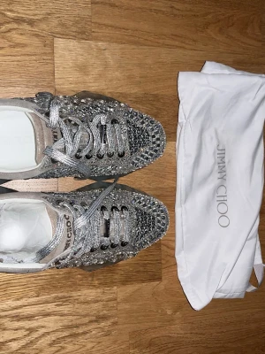 Jimmy Choo chunky rhinestone sneakers - Säljer ett par riktigt snygga sneakers från Jimmy Choo i silver med massor av glittrande stenar och paljetter. Skorna har silvriga skosnören och en genomskinlig sula. Perfekta för dig som vill sticka ut och älskar lyxiga detaljer. Nypris runt 5000. Aldrig använda då de är för små.
