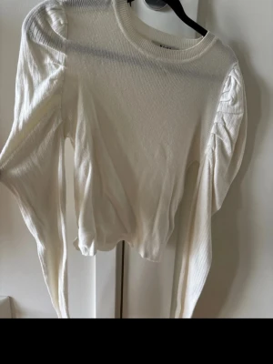Vit långärmad tröja  - Vit långärmad tröja med detaljer på axlarna, har en liten sminkfläck vid halskragen som kan ses på sista bilden