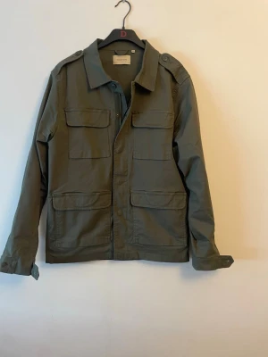 Grön utilityjacka/Overshirt - Snygg grön utilityjacka från Selected Homme med fyra stora fickor framtill och axelklaffar. Jackan har klassisk krage, knappar och dragkedja framtill. Perfekt för lager-på-lager och enkel att styla till olika outfits.