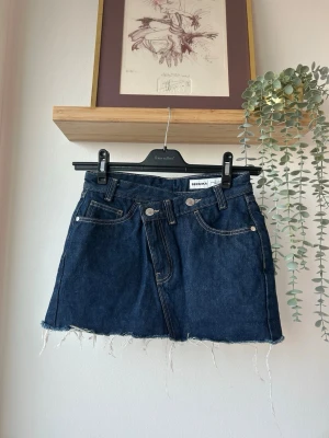 Mörkblå jeanskjol från Bershka - Mörkblå jeanskjol från Bershka med rå kant nertill och fickor fram och bak. Inbyggda shorts inuti som gör kjolen väldigt bekväm! Bara använd 1 gång. 