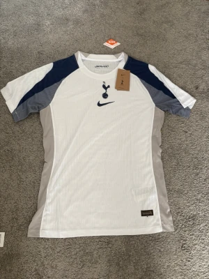 Tottenham Hotspur Nike matchtröja - Snygg vit Tottenham Hotspur matchtröja från Nike med mörkblå och grå detaljer på axlar och sidor. Tröjan har klubbens emblem och Nike-logga på bröstet. Tillverkad i lätt och ventilerande funktionsmaterial, perfekt för fotboll eller träning player edition .