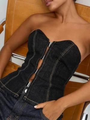 Svart denim korsett med metalldetaljer - Trendig svart korsett i denim med markerade sömmar och snygga metalldetaljer framtill. Axelbandslös och figurnära passform som ger en cool siluett. Perfekt att styla med jeans för en edgy look.