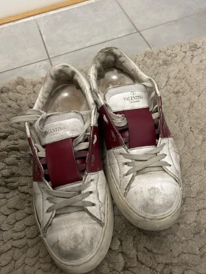 Valentino vita och vinröda sneakers - Säljer nu mina valentino open skor i storlek 37 med vinröda ränder. Skorna är slitna/smutsiga då de är använda vilket ni ser på bilderna men de är absolut användbara eftersom att jag endast säljer för jag måste köpa ett par skor till skolavslutningen. Kan SJÄLVKLART gå ner i pris så detta är bara ett start pris, kvitto finns och skorna är stora i storleken tycker jag då jag själv brukar ha 38!! Ska försöka göra rent de lite mer men tycker själv att de ser mer smutsiga ut på bild än verklighet! 