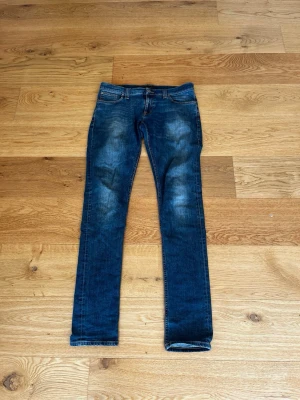 Mörkblå skinny jeans från Nudie - Snygga mörkblå skinny jeans från Nudie med klassisk femficksdesign och slitningar på låren. Jeansen har kontrastsömmar och broderade bakfickor. Tillverkade i stretchigt denim för en bekväm passform. W30 L36. Dom är stora i midjan!
