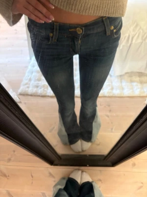 Mörkblå bootcut jeans med låg midja - Snygga mörkblå bootcut jeans med låg midja och klassiska fickor fram och bak. Jeansen har guldfärgade detaljer och en lätt tvättad look. Perfekta för dig som gillar en retrostil och vill ha ett par jeans med lite utsvängda ben. De har blivit sydda till bootcut!!